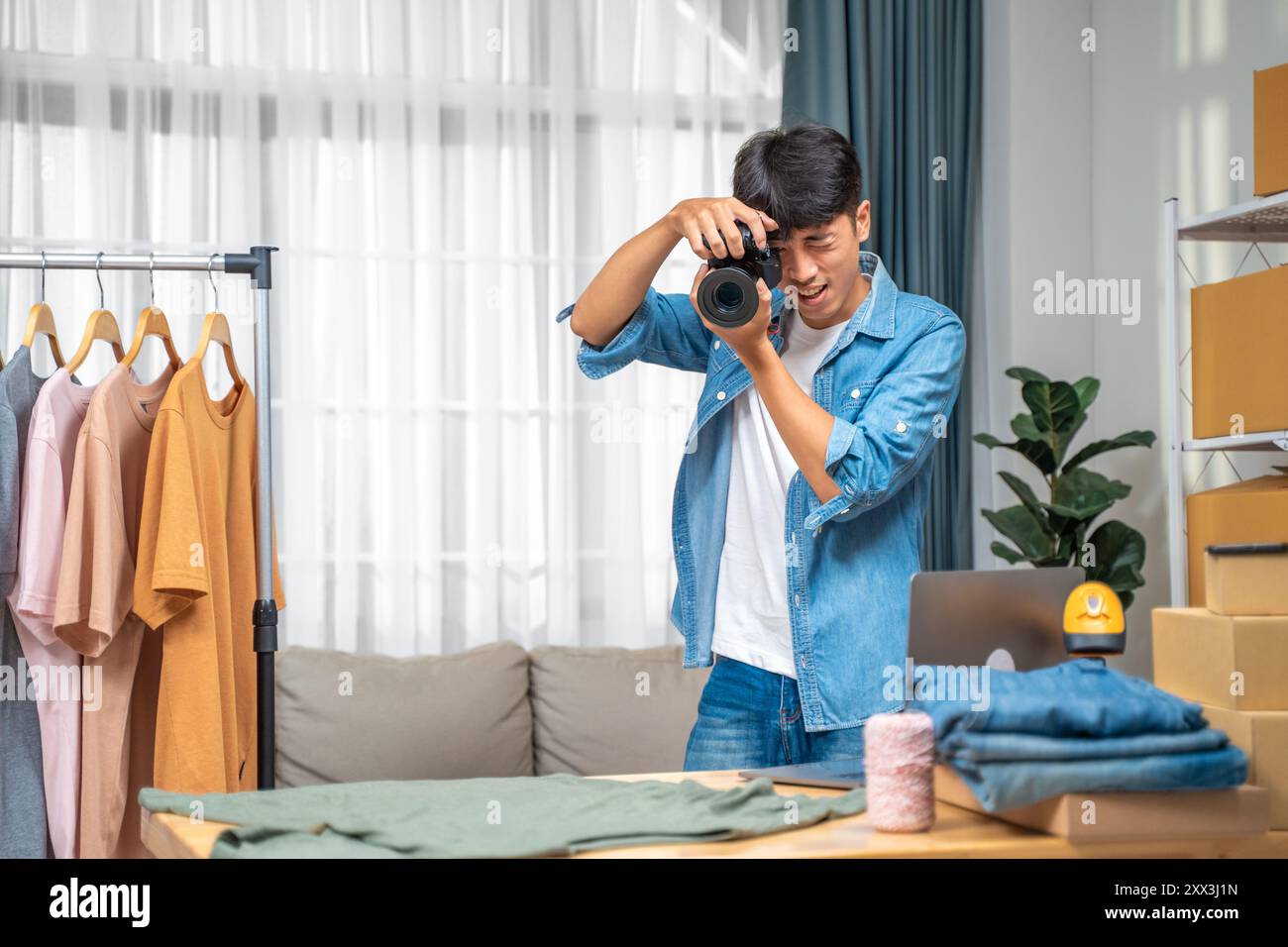 Giovane venditore online che scatta foto del suo prodotto per camicia da utilizzare sul suo sito Web e recensione online presso il suo studio di casa Foto Stock
