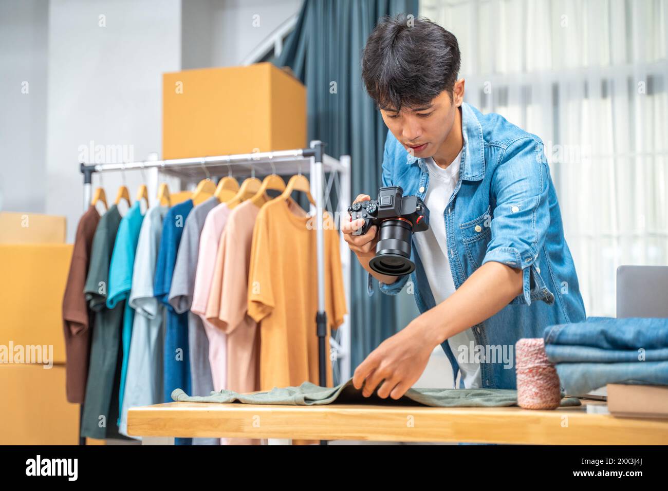 Giovane venditore online che scatta foto del suo prodotto per camicia da utilizzare sul suo sito Web e recensione online presso il suo studio di casa Foto Stock