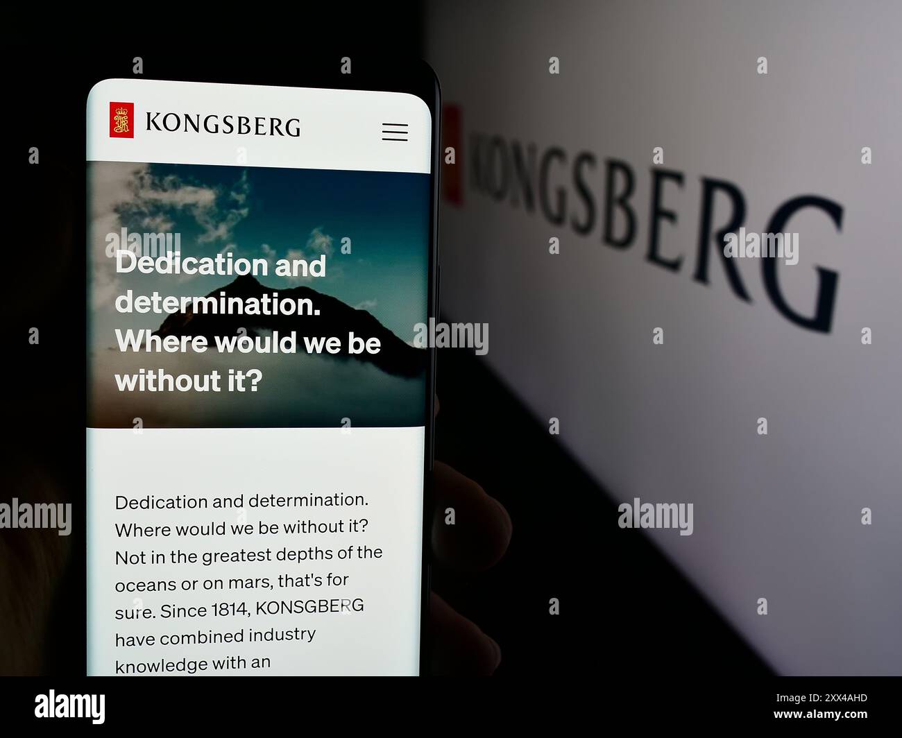 Persona che detiene lo smartphone con pagina web della società norvegese Kongsberg Gruppen ASA davanti al logo aziendale. Messa a fuoco al centro del display del telefono. Foto Stock