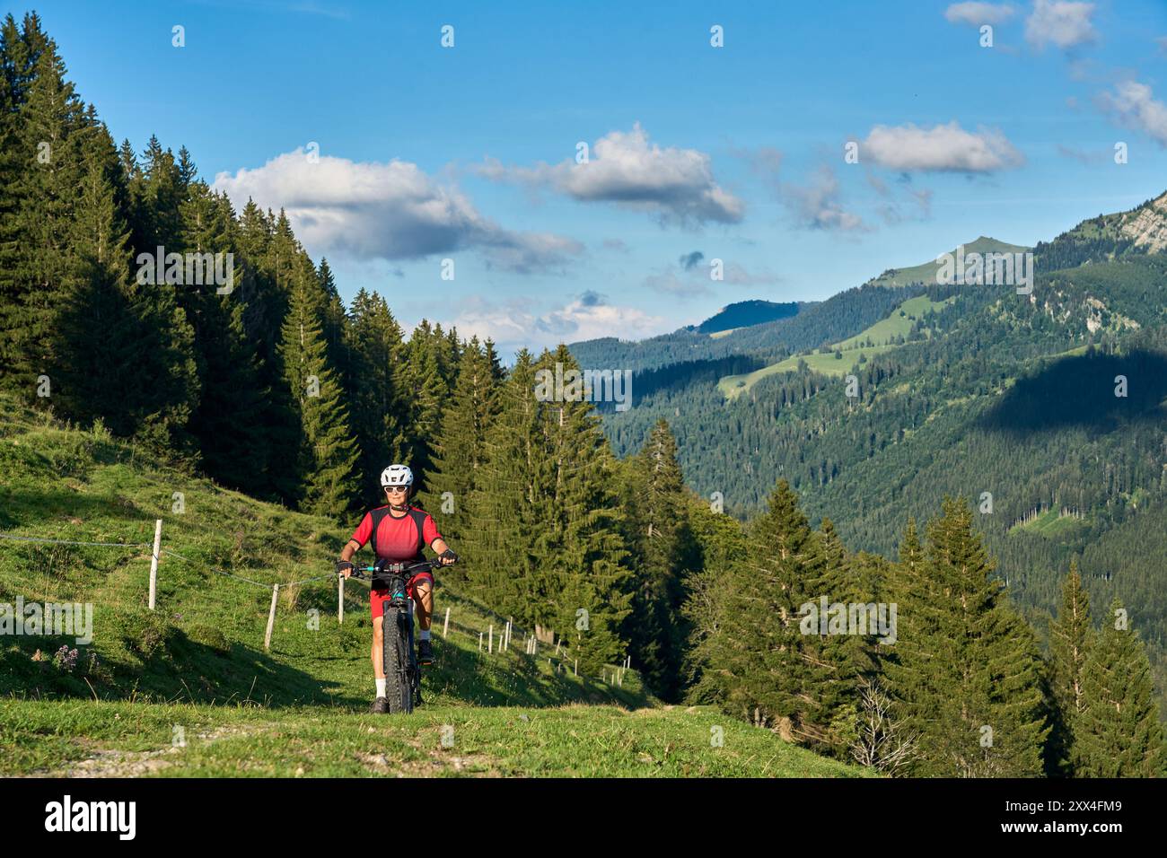 Bella donna anziana in sella alla sua mountain bike elettrica e godendosi la vista spettacolare sulle alpi Allgau sotto la catena montuosa Nagelfluh accanto Foto Stock