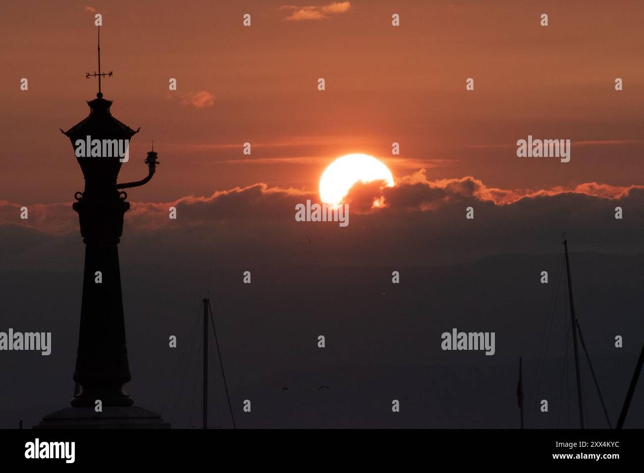 Splendido tramonto con un grande sole arancione parzialmente oscurato dalle nuvole all'orizzonte. La silhouette di un lampione è in primo piano. Foto Stock