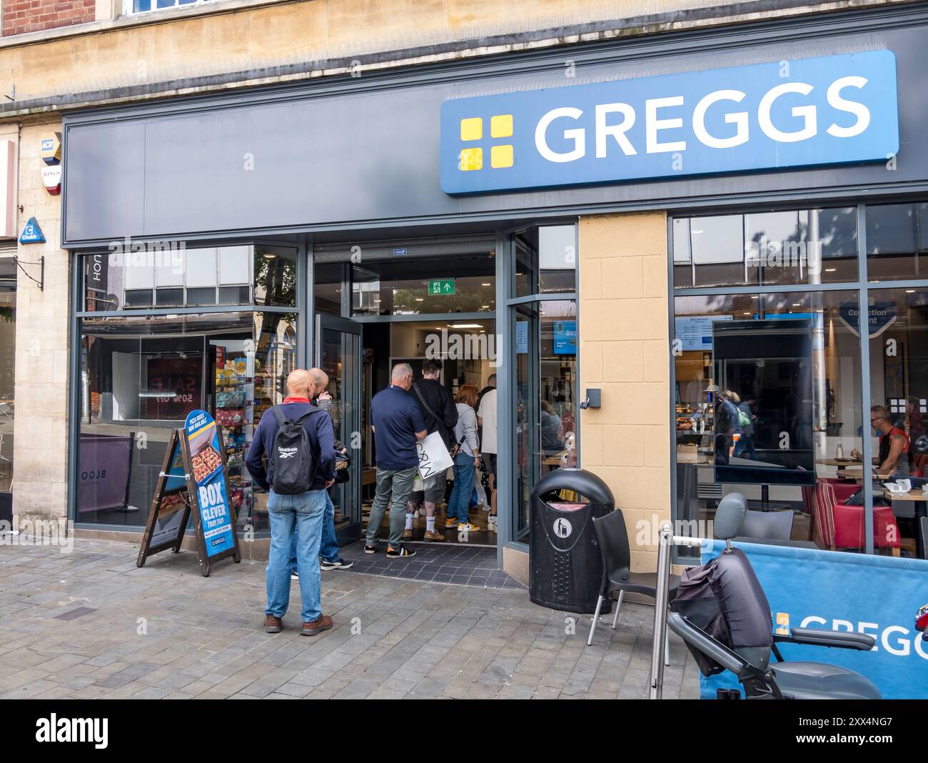 Persone in coda per essere servite al negozio di alimentari e bevande Greggs, High Street, Lincoln City, Lincolnshire, Inghilterra, REGNO UNITO Foto Stock