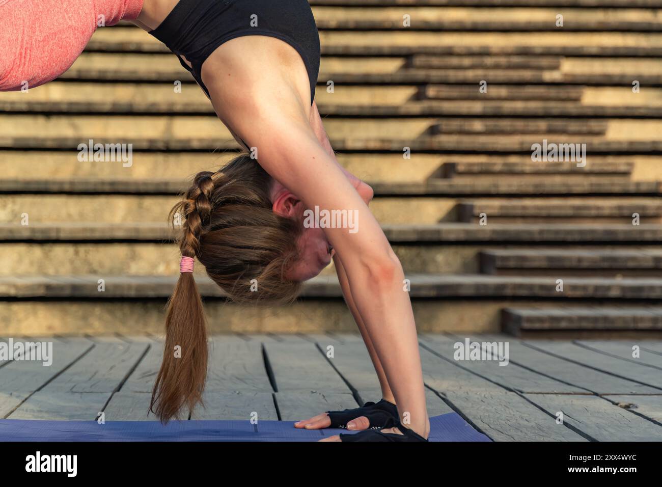 Giovane donna rossa che pratica yoga all'aperto su una piattaforma di legno. È in posa sul ponte, allungando la schiena e l'addome mentre si appoggia sulla sua h Foto Stock