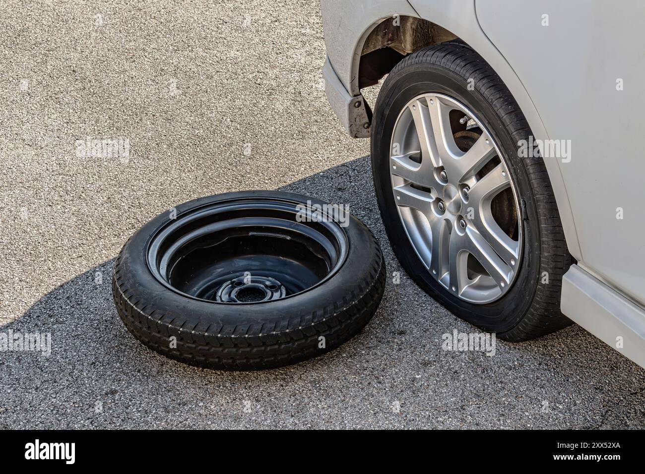 Immagine orizzontale di uno pneumatico sgonfio e della ruota di scorta su una piccola auto bianca. Foto Stock