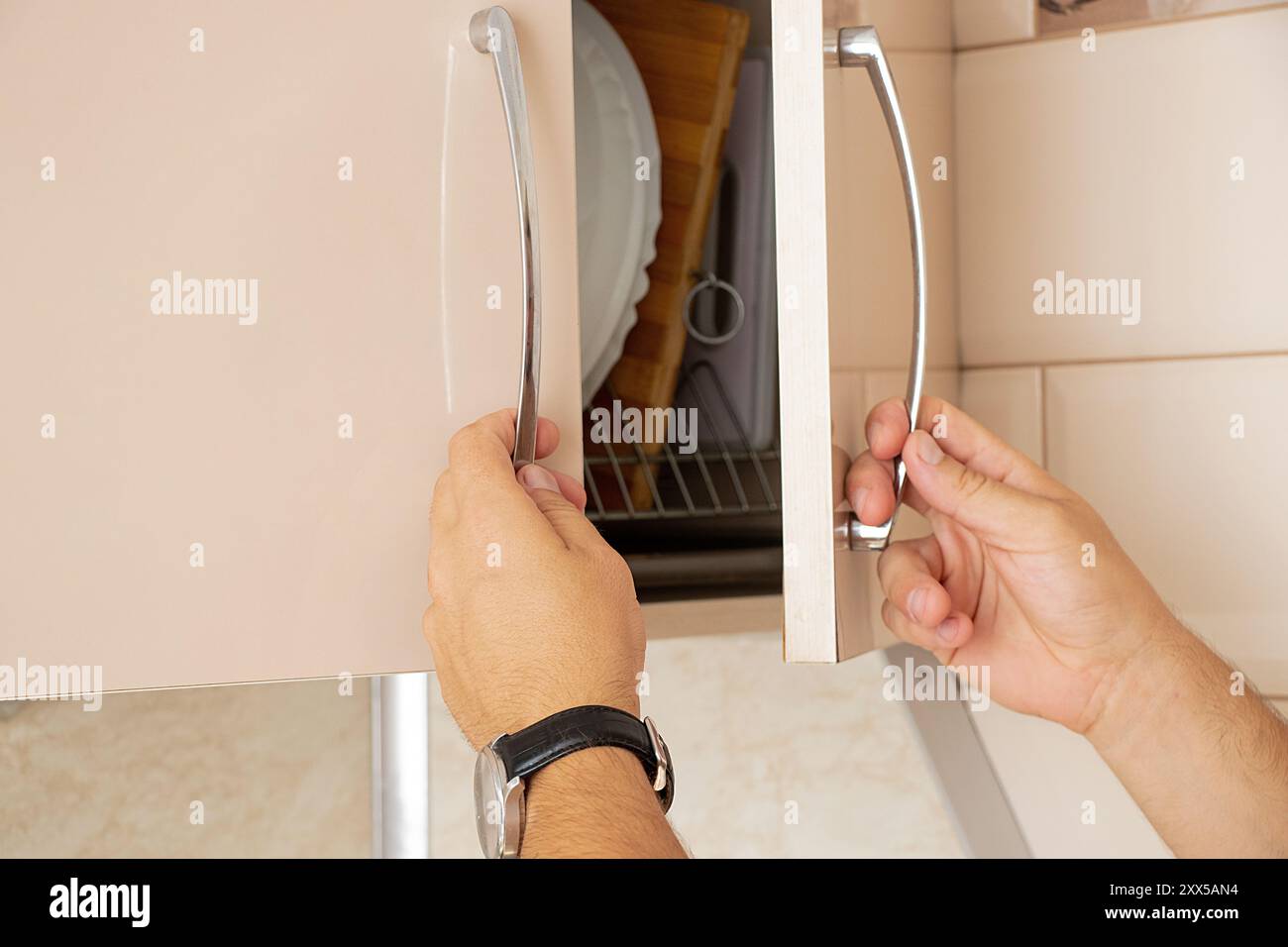 Mani maschili che aprono l'armadio da cucina beige in cucina nell'appartamento, mobili da cucina Foto Stock