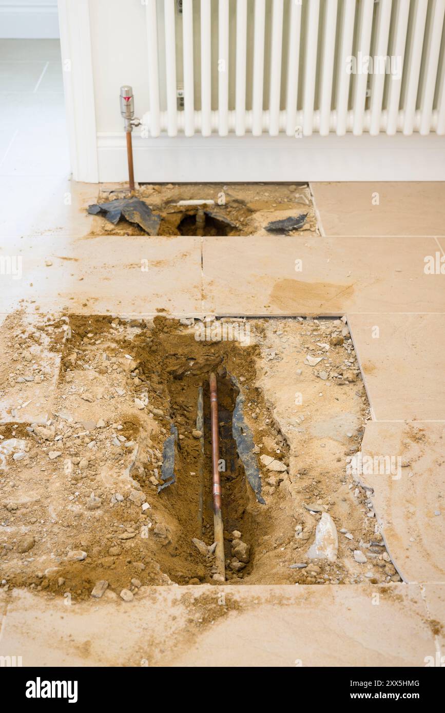 Tubazioni di riscaldamento centralizzato domestico esposte sotto un pavimento piastrellato dopo aver riparato una perdita d'acqua in una casa nel Regno Unito Foto Stock