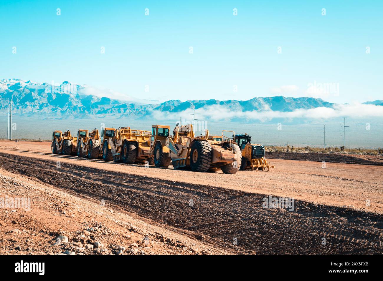 Una flotta di traslocatori di terra prepara terreni desertici aridi per lo sviluppo di nuove abitazioni. Le montagne si insinuano sullo sfondo mentre le attrezzature da costruzione si trasformano Foto Stock