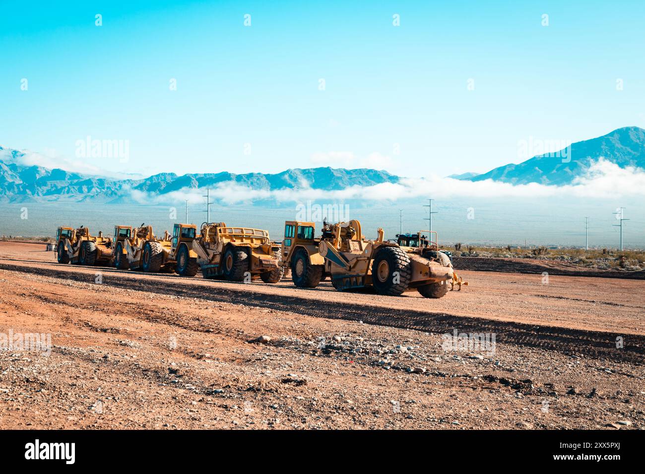 Una flotta di traslocatori di terra prepara terreni desertici aridi per lo sviluppo di nuove abitazioni. Le montagne si insinuano sullo sfondo mentre le attrezzature da costruzione si trasformano Foto Stock