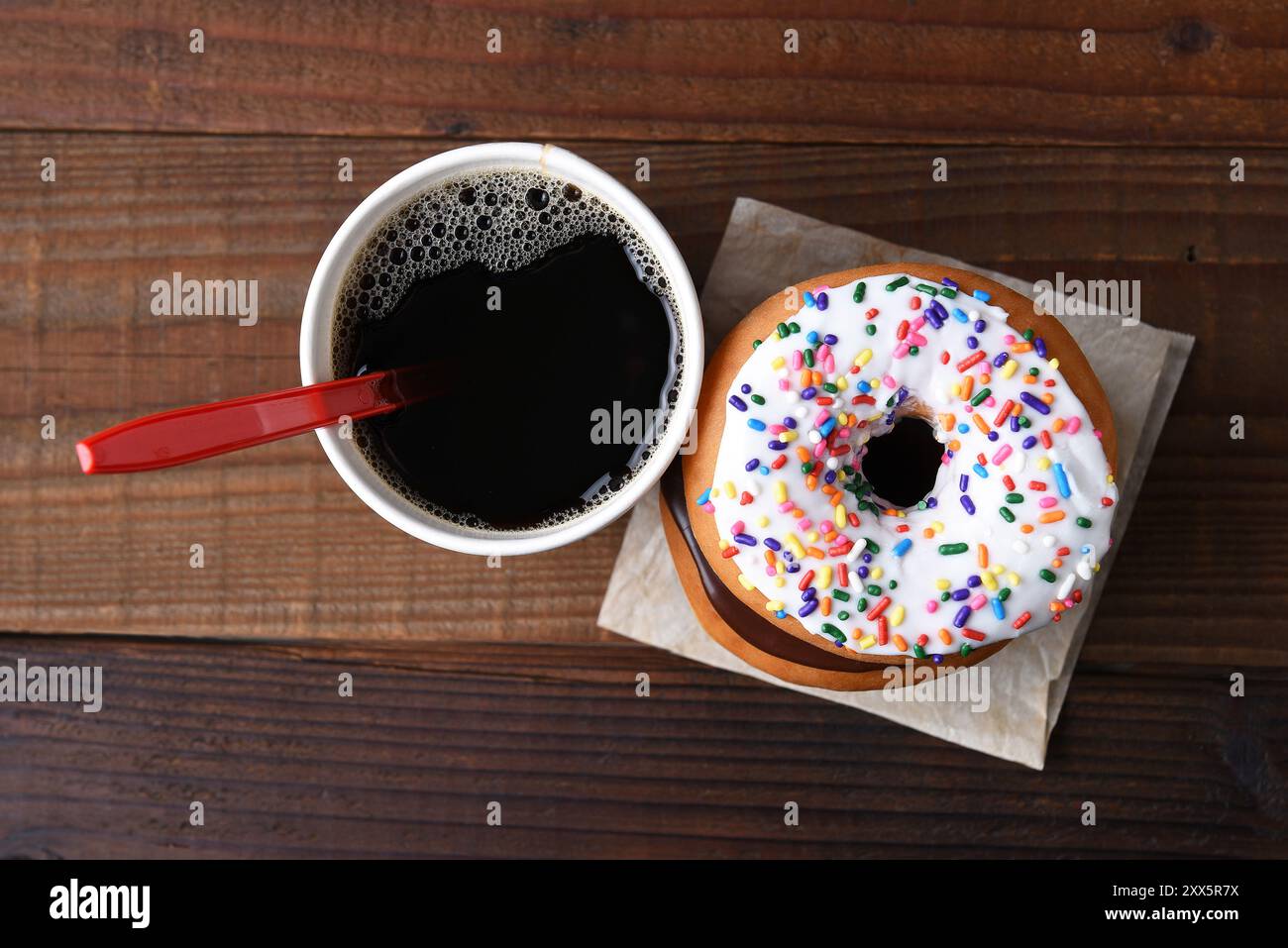 Vista ad angolo alto di una tazza di carta di caffè caldo appena preparato accanto a una pila di ciambelle. Foto Stock