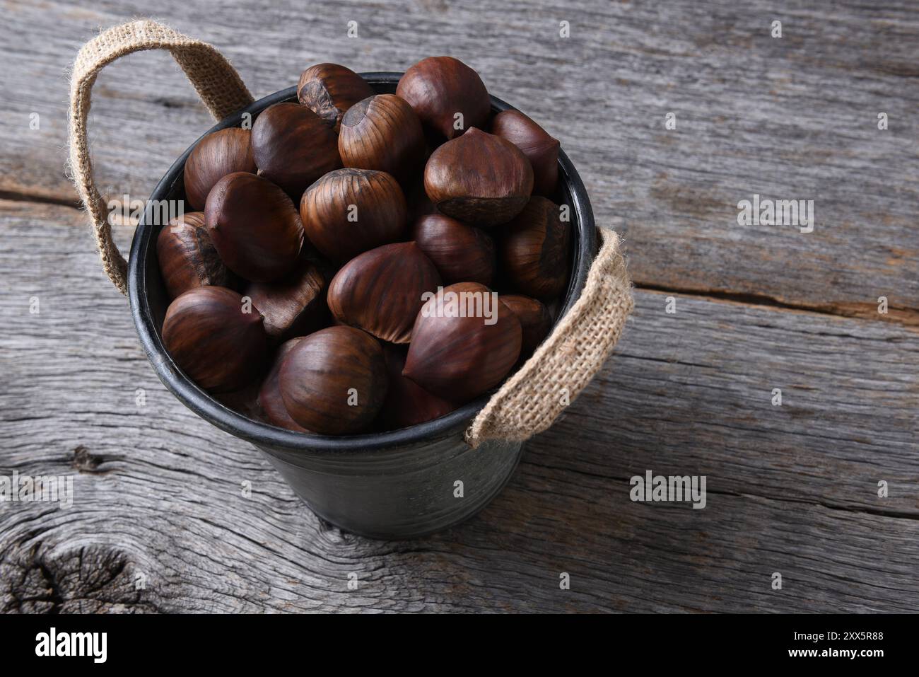 Un secchio pieno di castagne crude fresche. Foto Stock