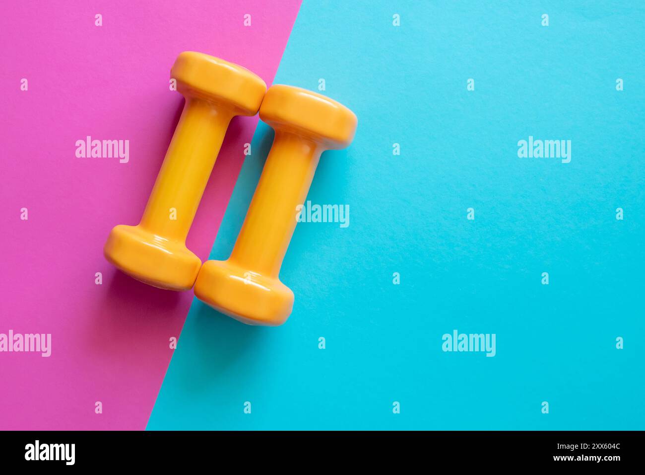 Due manubri arancioni su sfondo rosa e blu con spazio per le copie. Uno strumento per l'allenamento, lo sport e l'attività in estate. Foto Stock