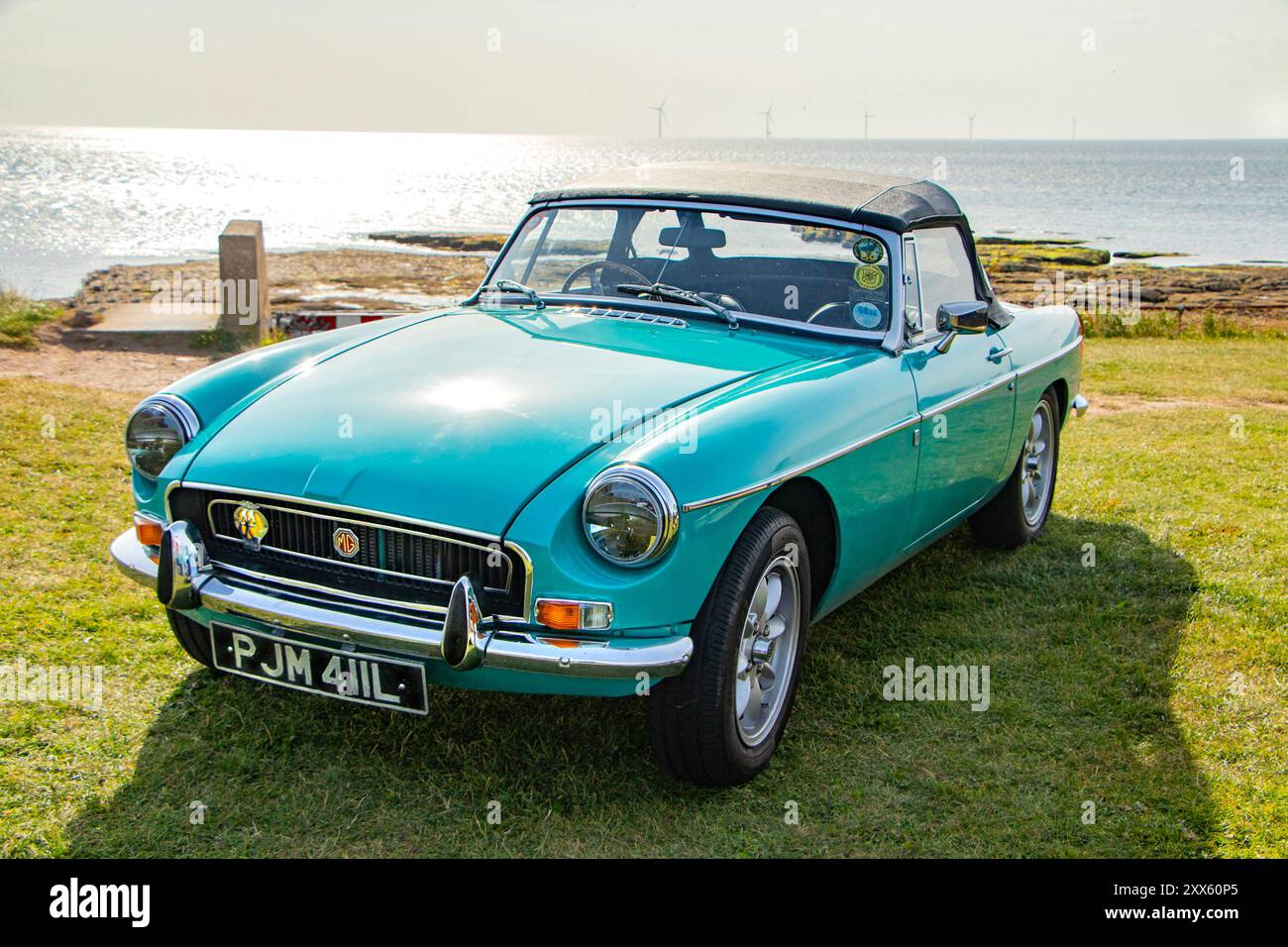 Un'auto sportiva MG decappottabile d'epoca verde menta parcheggiata su un lussureggiante prato verde sul mare con una vista panoramica dell'oceano sullo sfondo. Foto Stock