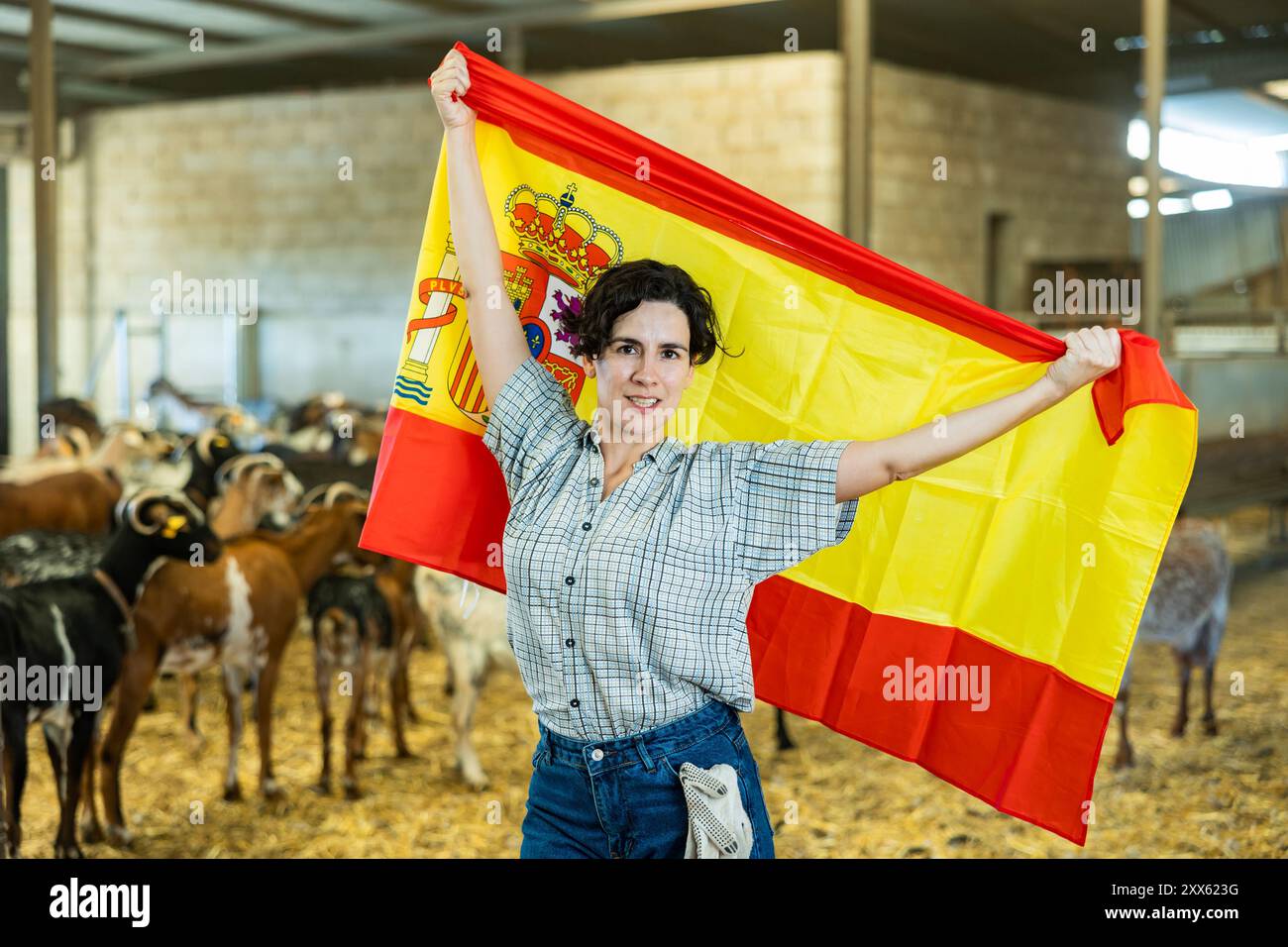 Felice femmina contadina in piedi in capannone di capra con bandiera spagnola Foto Stock