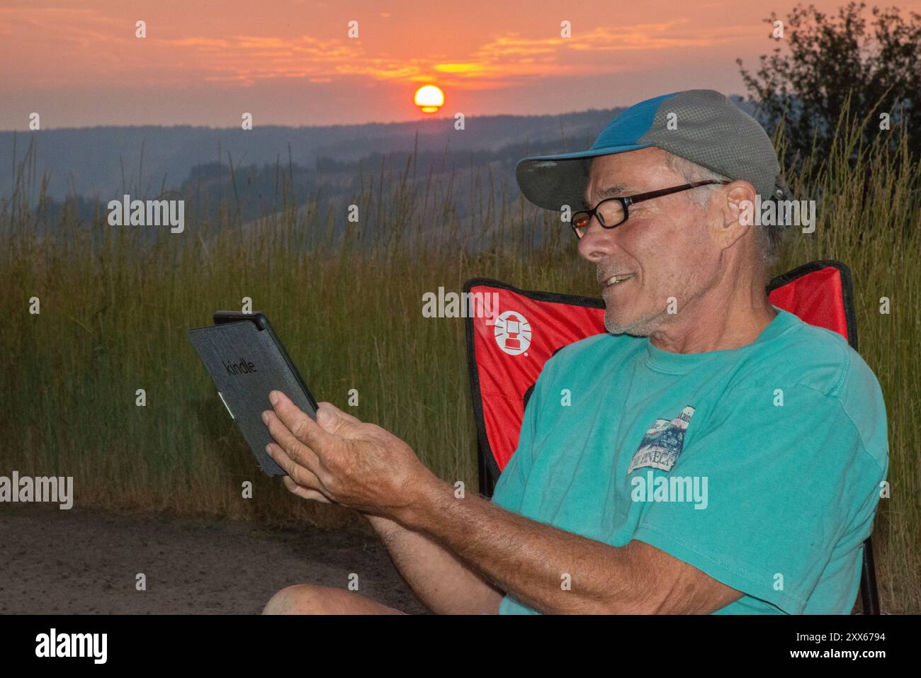 Un maschio adulto si rilassa mentre legge su un libro Kindle a Spring Mountain nella catena montuosa Blue Mountain dell'Oregon centrale. Foto Stock