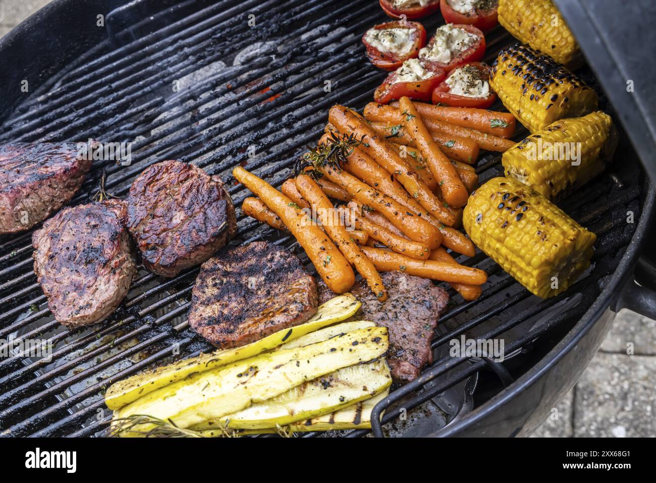 Vegetariano o con carne: I barbecue sono di tendenza. Verdure come carote, pomodori e zucchine e bistecche su un bollitore grill. Germe Foto Stock