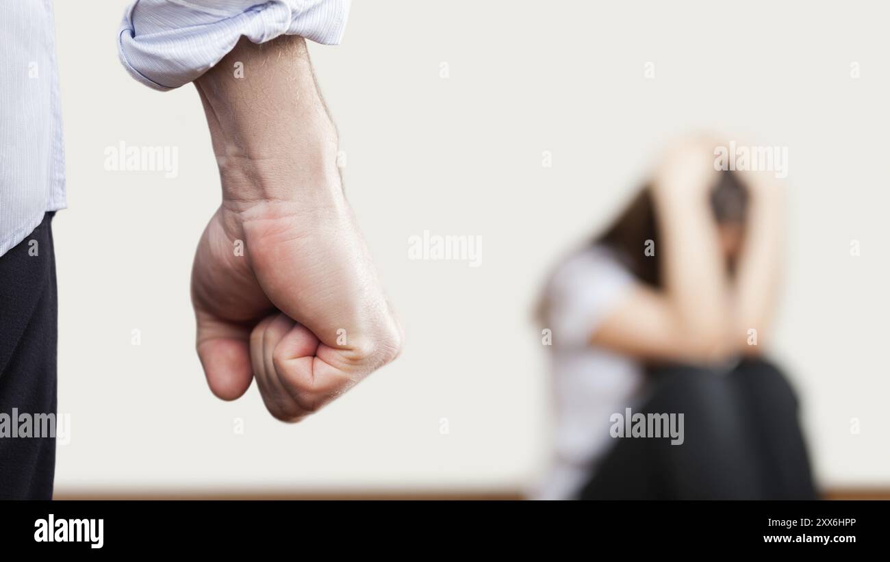 Concetto di violenza familiare e aggressione, uomo furioso arrabbiato ha alzato pugno di punizione per una donna spaventata o terrorizzata seduta all'angolo del muro Foto Stock