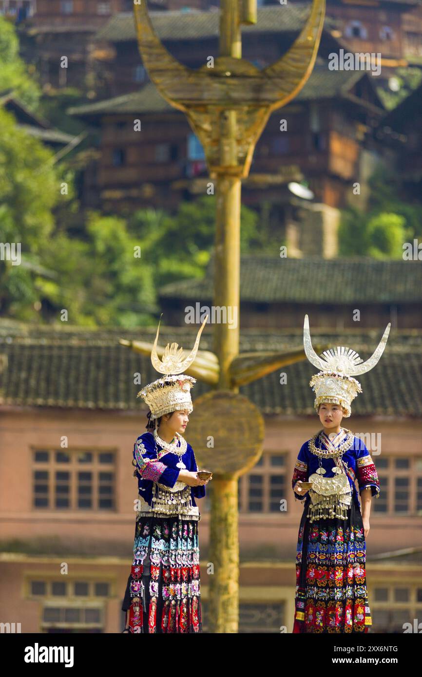 Xijiang, Cina, 15 settembre 2007: Due donne Miao della minoranza etnica indossano abiti tradizionali e copricapo d'argento al palo di legno a della piazza della città Foto Stock