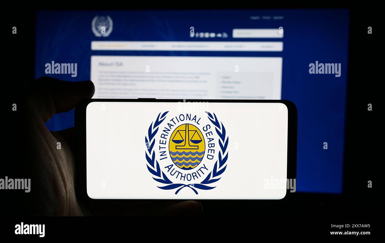 Persona che possiede un telefono cellulare con il logo dell’organizzazione International Seabed Authority (ISA) di fronte alla pagina web aziendale. Mettere a fuoco il display del telefono. Foto Stock