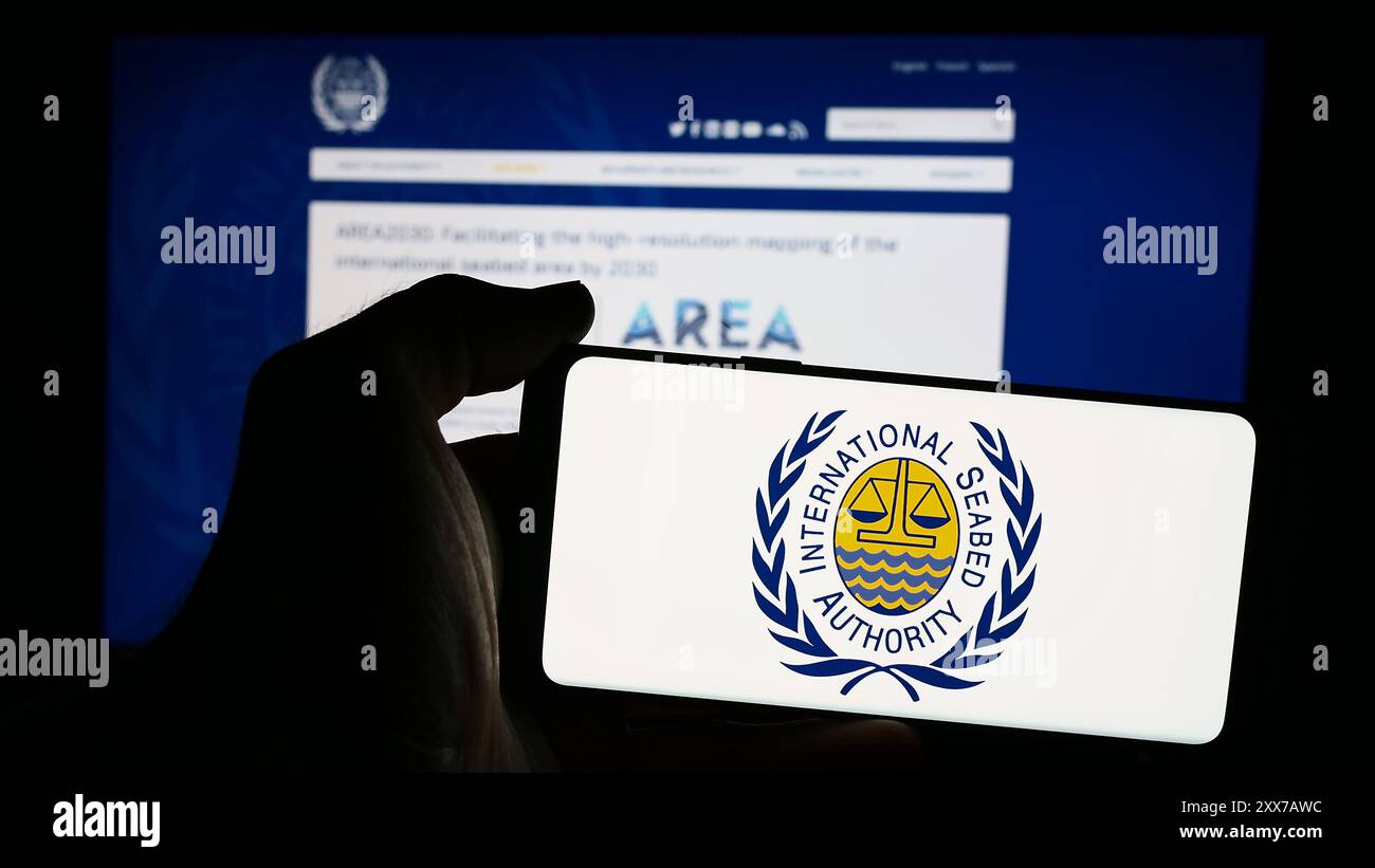 Persona che detiene un cellulare con il logo dell’organizzazione International Seabed Authority (ISA) di fronte alla pagina web aziendale. Mettere a fuoco il display del telefono. Foto Stock