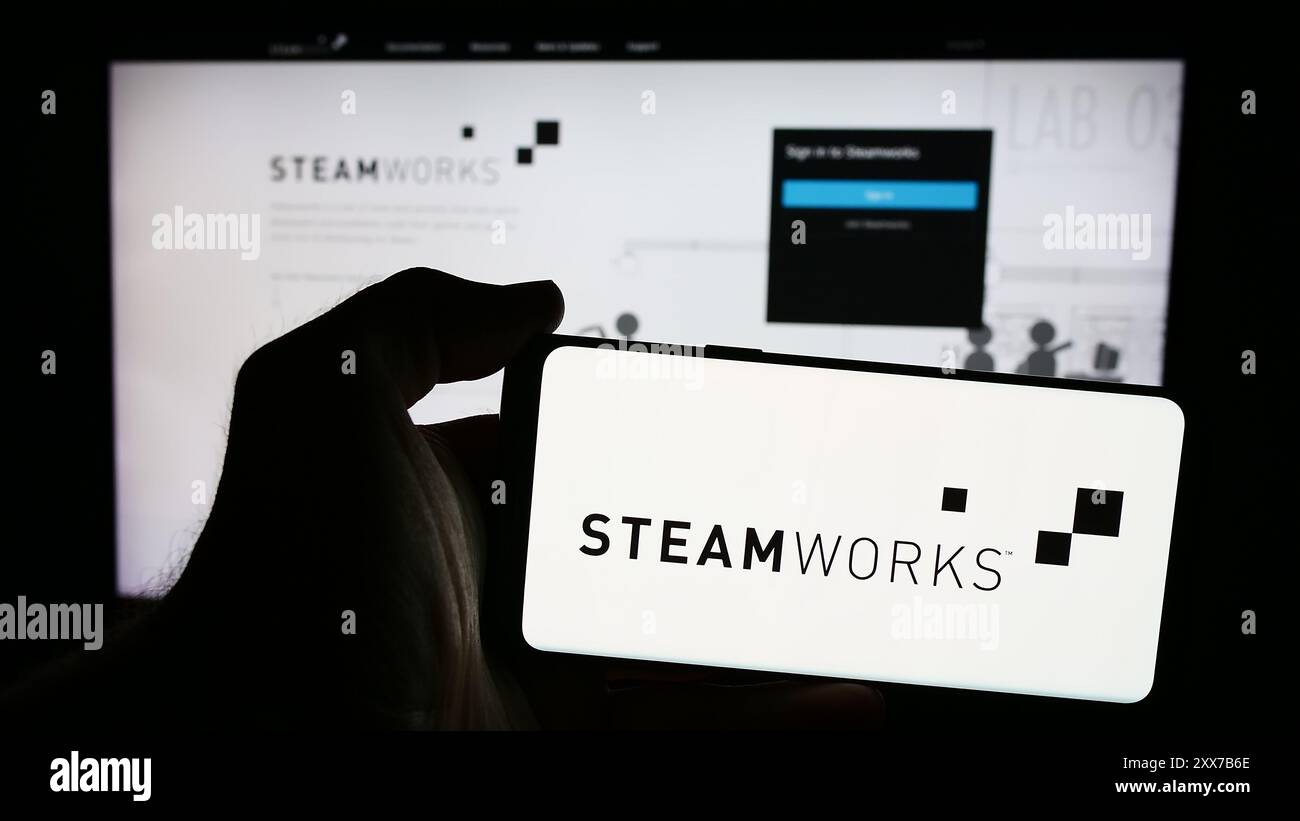 Persona che possiede lo smartphone con il logo dell'interfaccia di programmazione dell'applicazione Steamworks (Steam) davanti al sito Web. Mettere a fuoco il display del telefono. Foto Stock