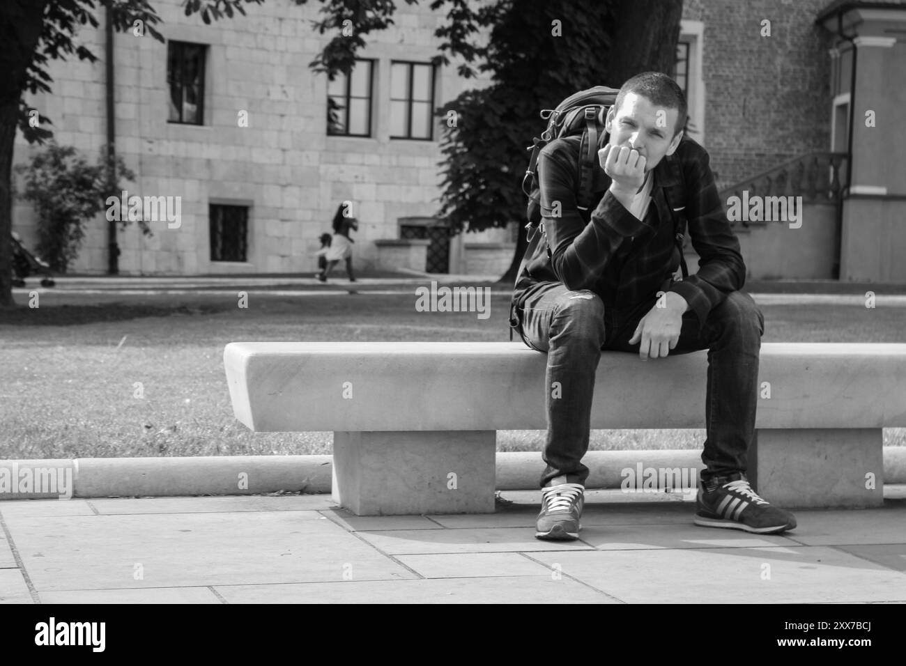 Uomo solo seduto sulla panchina, monocromatico. Turista con zaino e scarpe adidas che pensano sulla panchina nel parco, in bianco e nero. Stile di vita attivo. Foto Stock