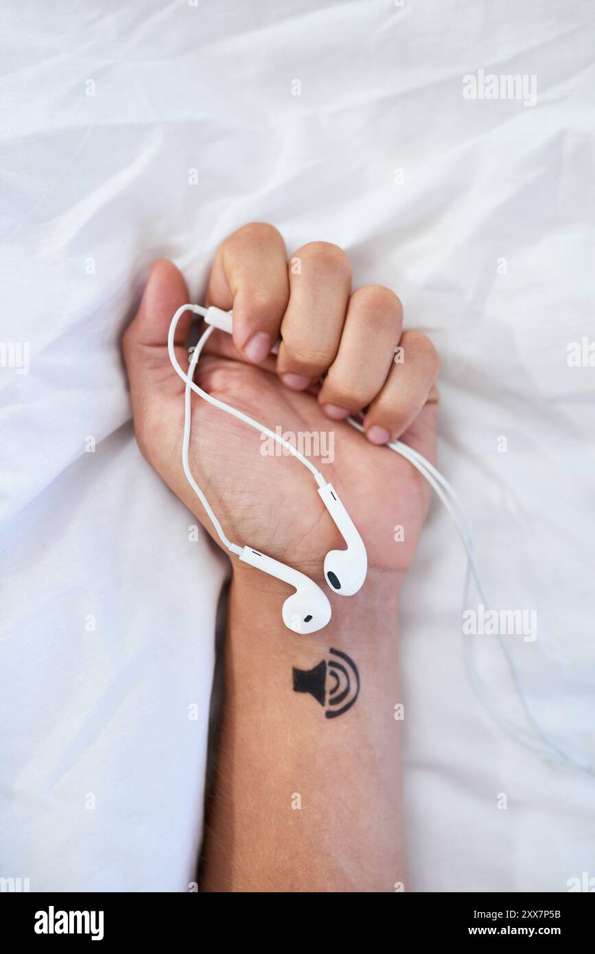 Mani, persona e letto con auricolari per ascoltare musica, audio per curare corpo, anima e mente. Volume, audio e radio in pausa nella camera da letto di casa a. Foto Stock