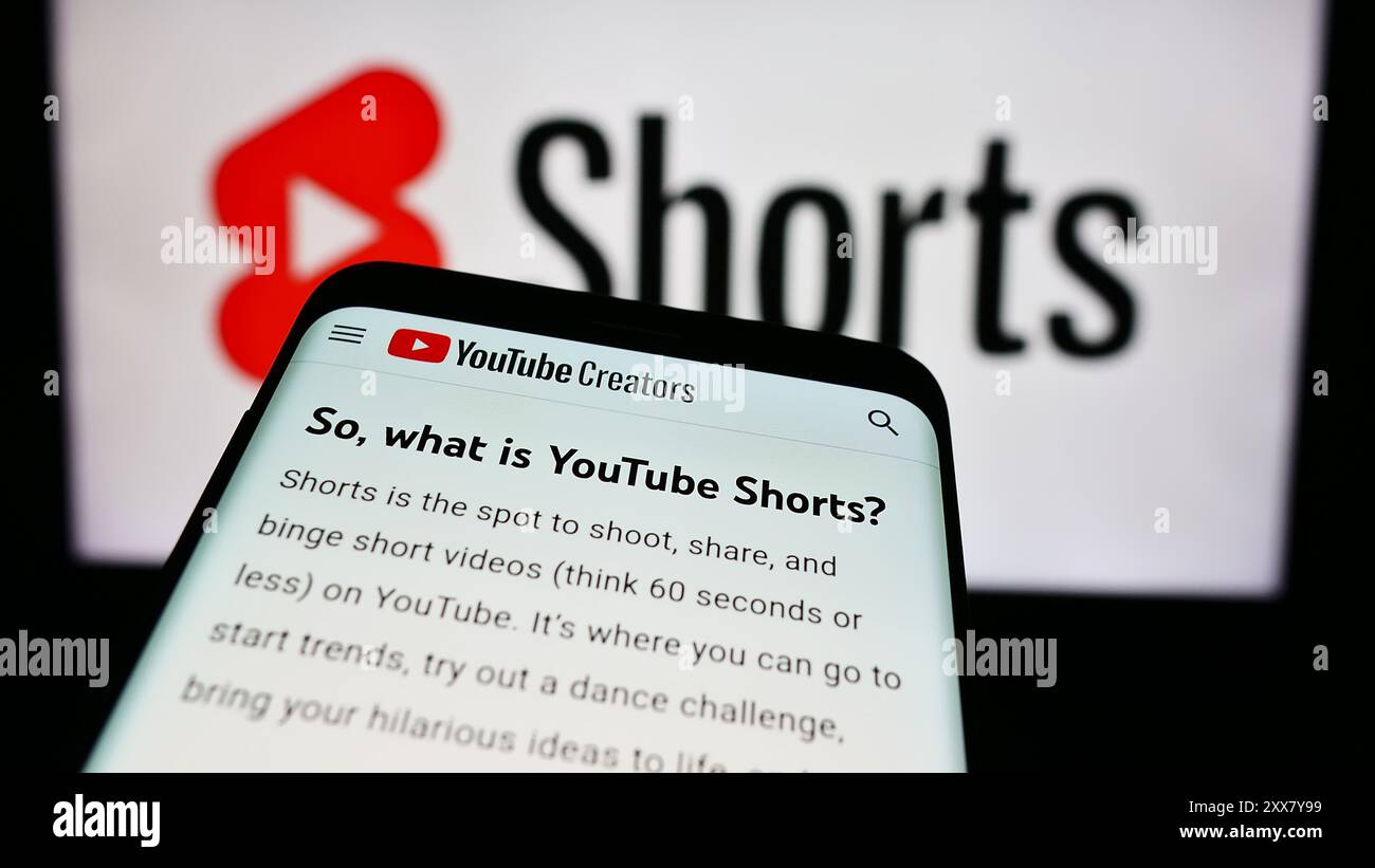 Smartphone con sito Web di un breve servizio di condivisione di video YouTube Short davanti al logo aziendale. Mettere a fuoco in alto a sinistra sul display del telefono. Foto Stock