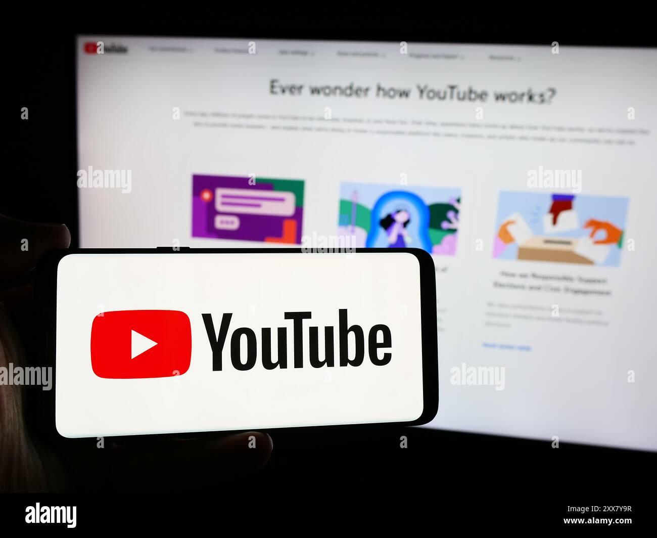 Persona che possiede uno smartphone con il logo della società statunitense di piattaforme di condivisione video online YouTube davanti al sito web. Mettere a fuoco il display del telefono. Foto Stock