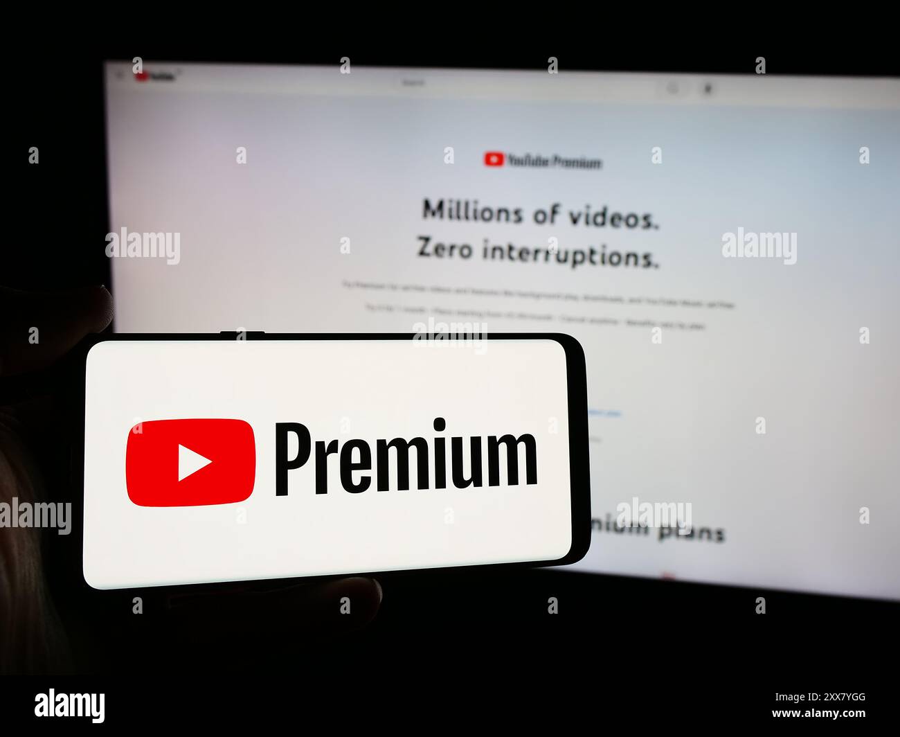 Persona con smartphone con logo del servizio di abbonamento streaming video YouTube Premium davanti al sito Web. Mettere a fuoco il display del telefono. Foto Stock