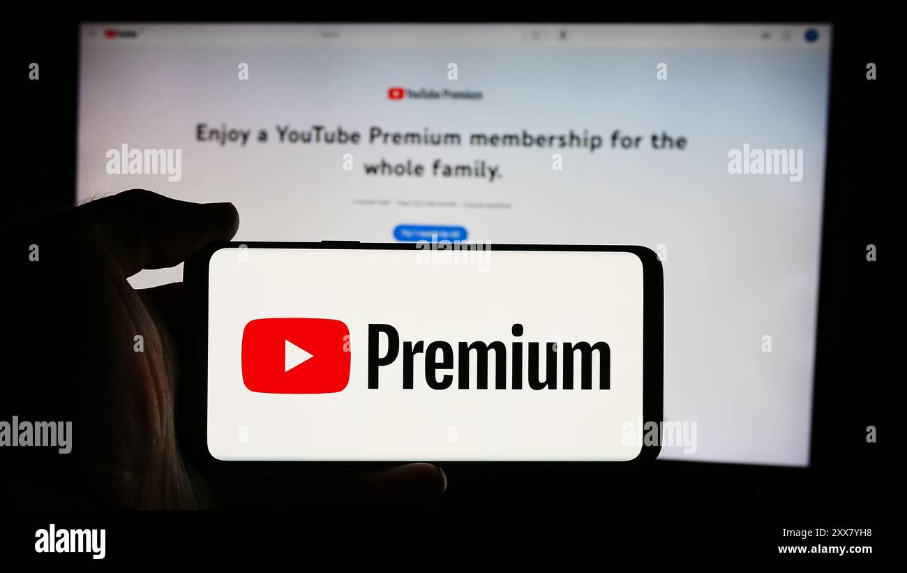 Persona che detiene un cellulare con il logo del servizio di abbonamento streaming video YouTube Premium davanti alla pagina Web aziendale. Mettere a fuoco il display del telefono. Foto Stock