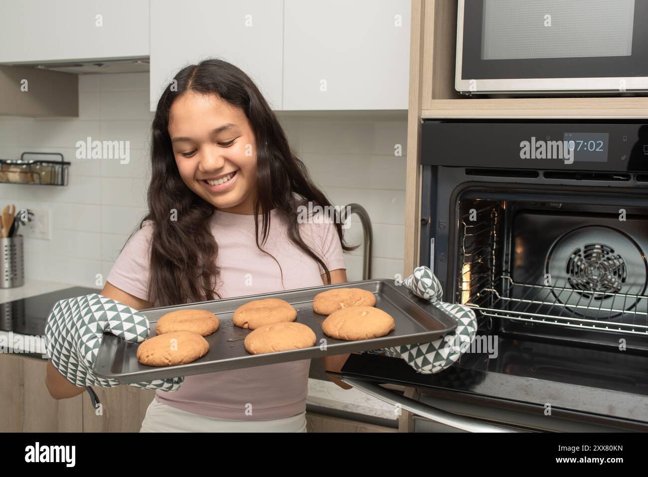 Ragazza che rimuove dal forno il vassoio dei biscotti appena sfornati Foto Stock