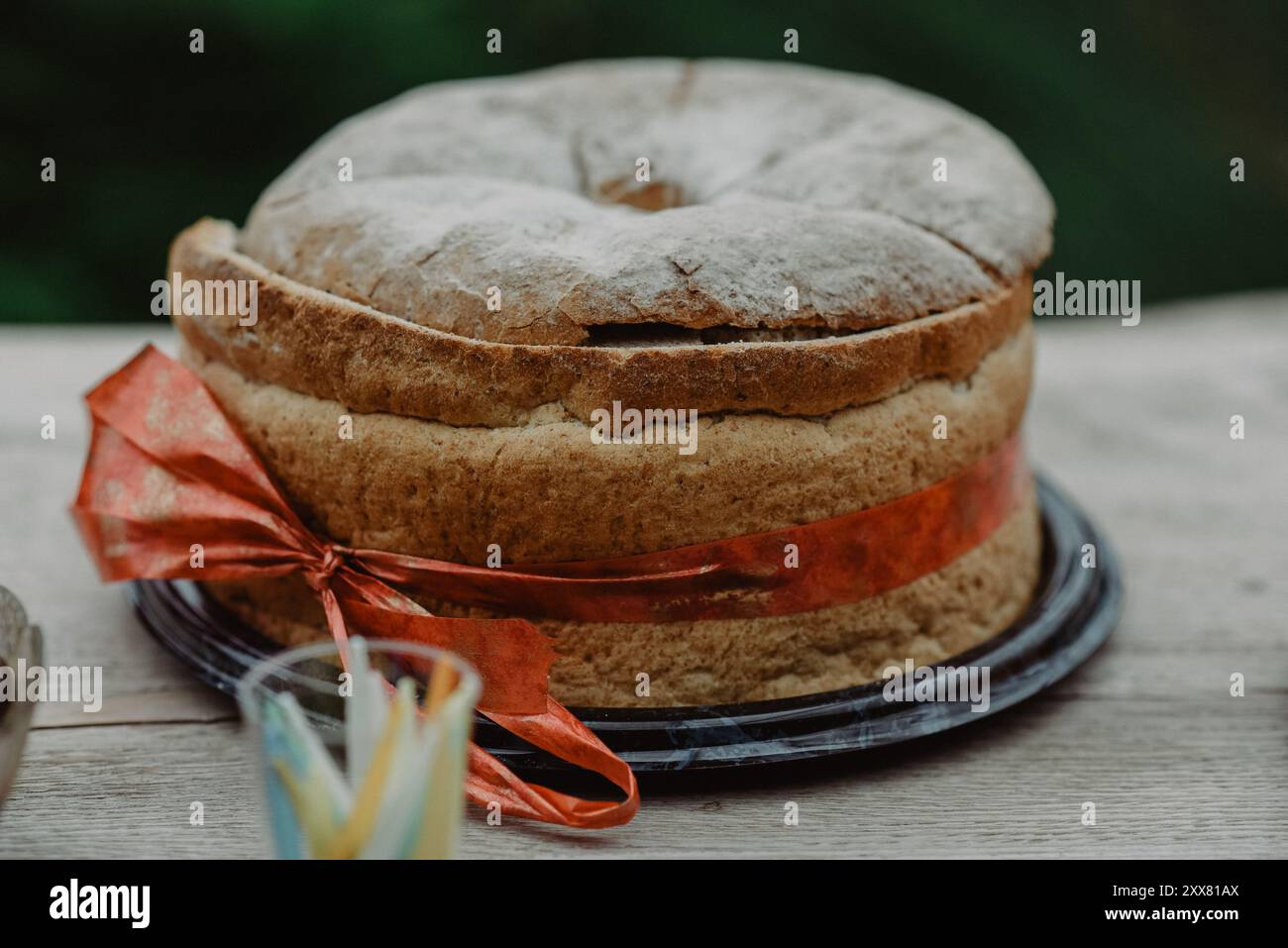 Pane da festa rotondo con un nastro rosso posto su un tavolo di legno Foto Stock