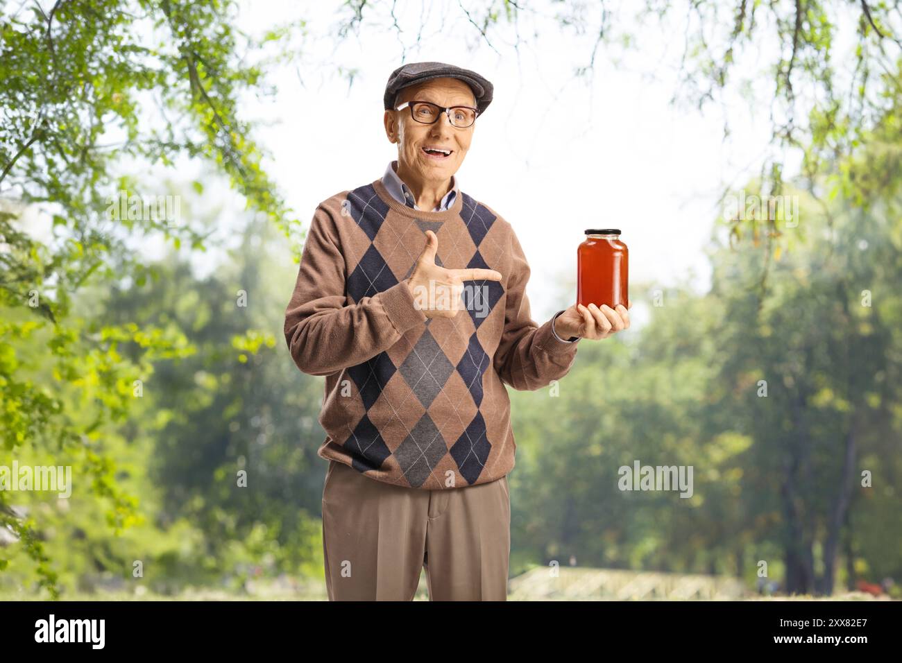 Uomo anziano che tiene in mano un vaso di miele in natura e punta Foto Stock