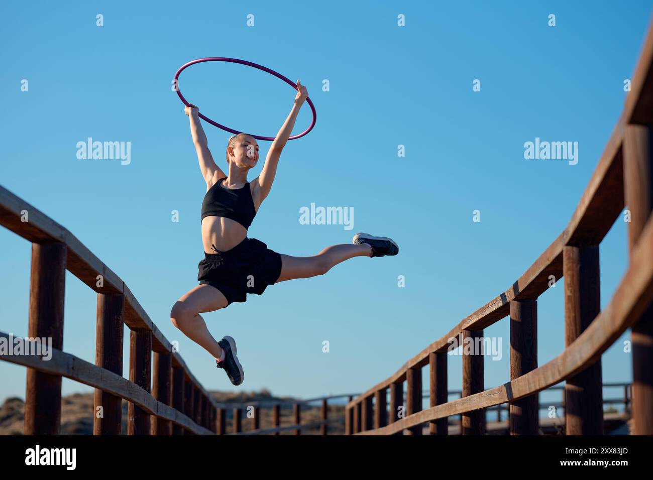 Una ballerina esegue un gioioso salto con un hula hoop su un ponte di legno Foto Stock