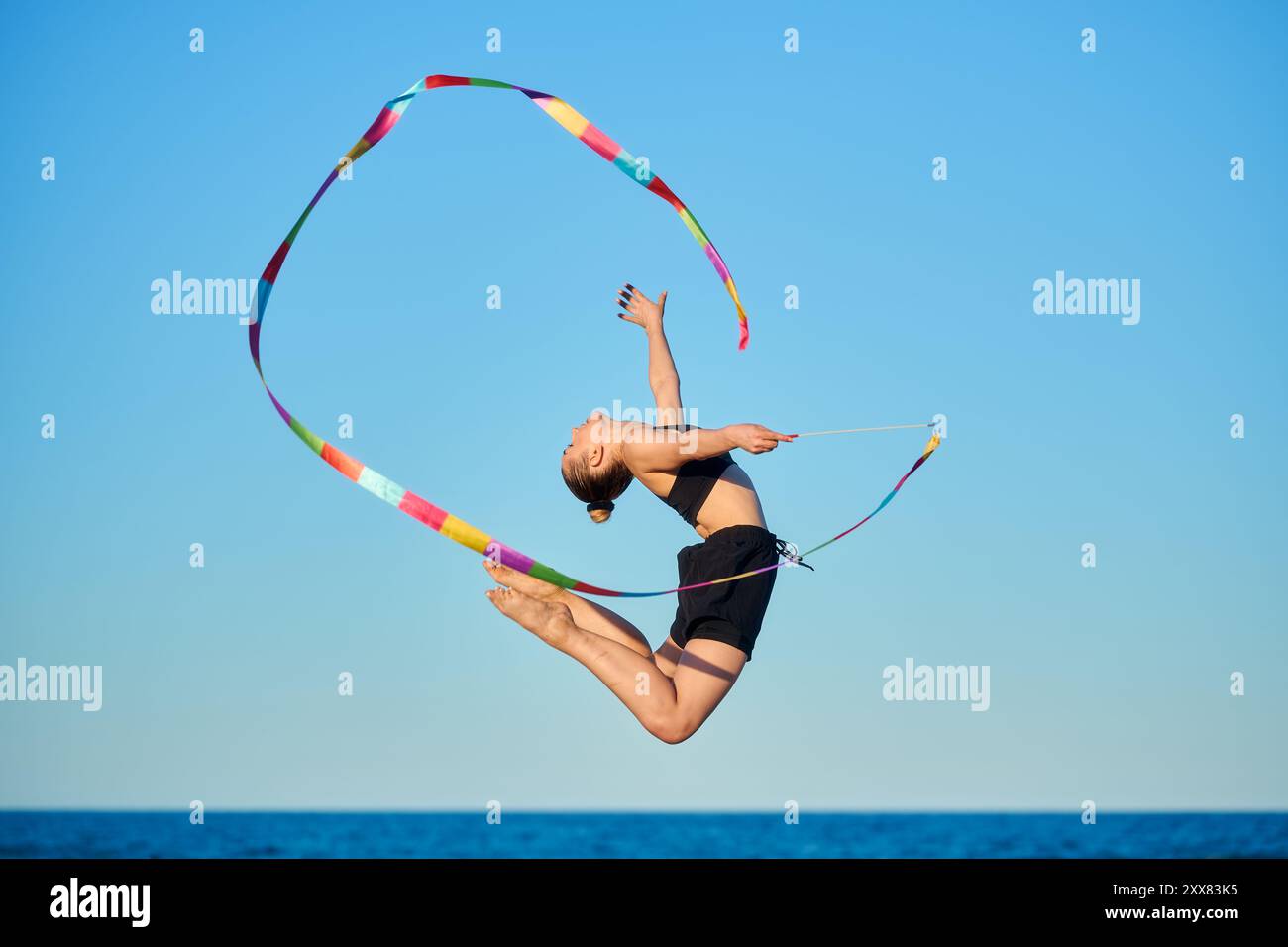 Giovane donna che esegue ginnastica ritmica con il nastro su una spiaggia Foto Stock