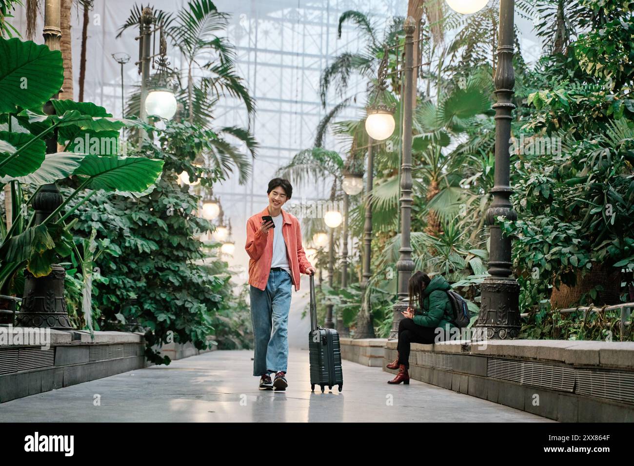 giovane asiatico che cammina e guarda il suo smartphone con una borsa da viaggio Foto Stock