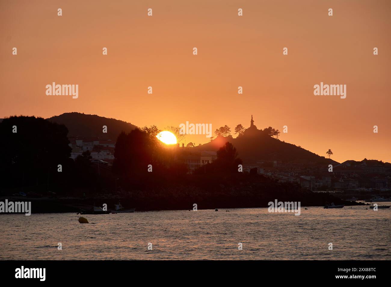Tramonto unico a Ladeira Beach, dove il sole tramonta dietro un albero solitario, creando una silhouette impressionante contro il cielo serale Foto Stock