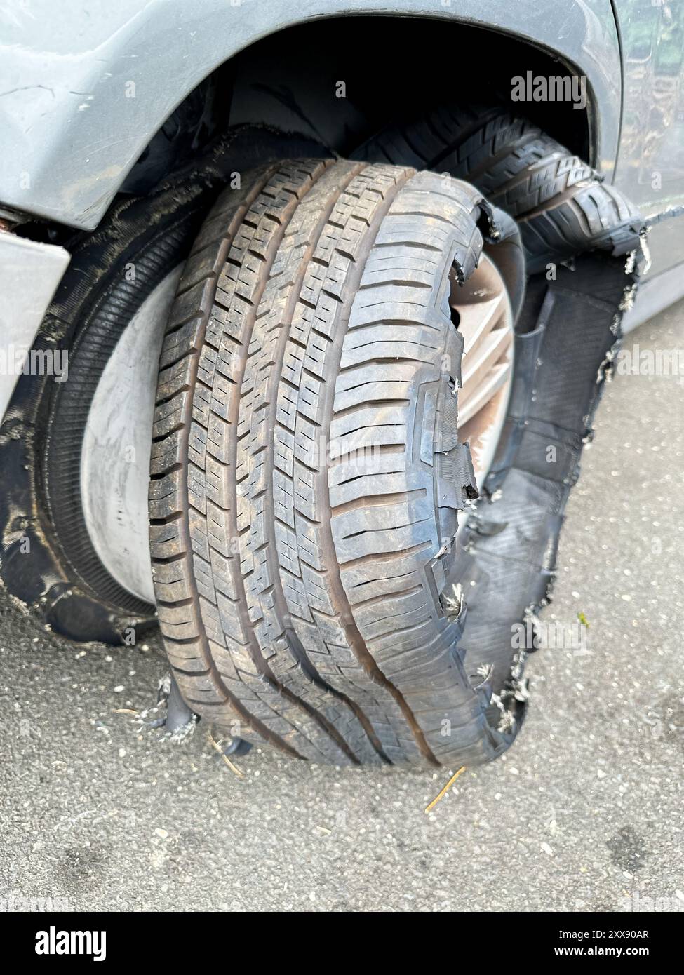 Un veicolo presenta uno pneumatico sgonfio che mostra danni estesi mentre è parcheggiato su una strada Foto Stock