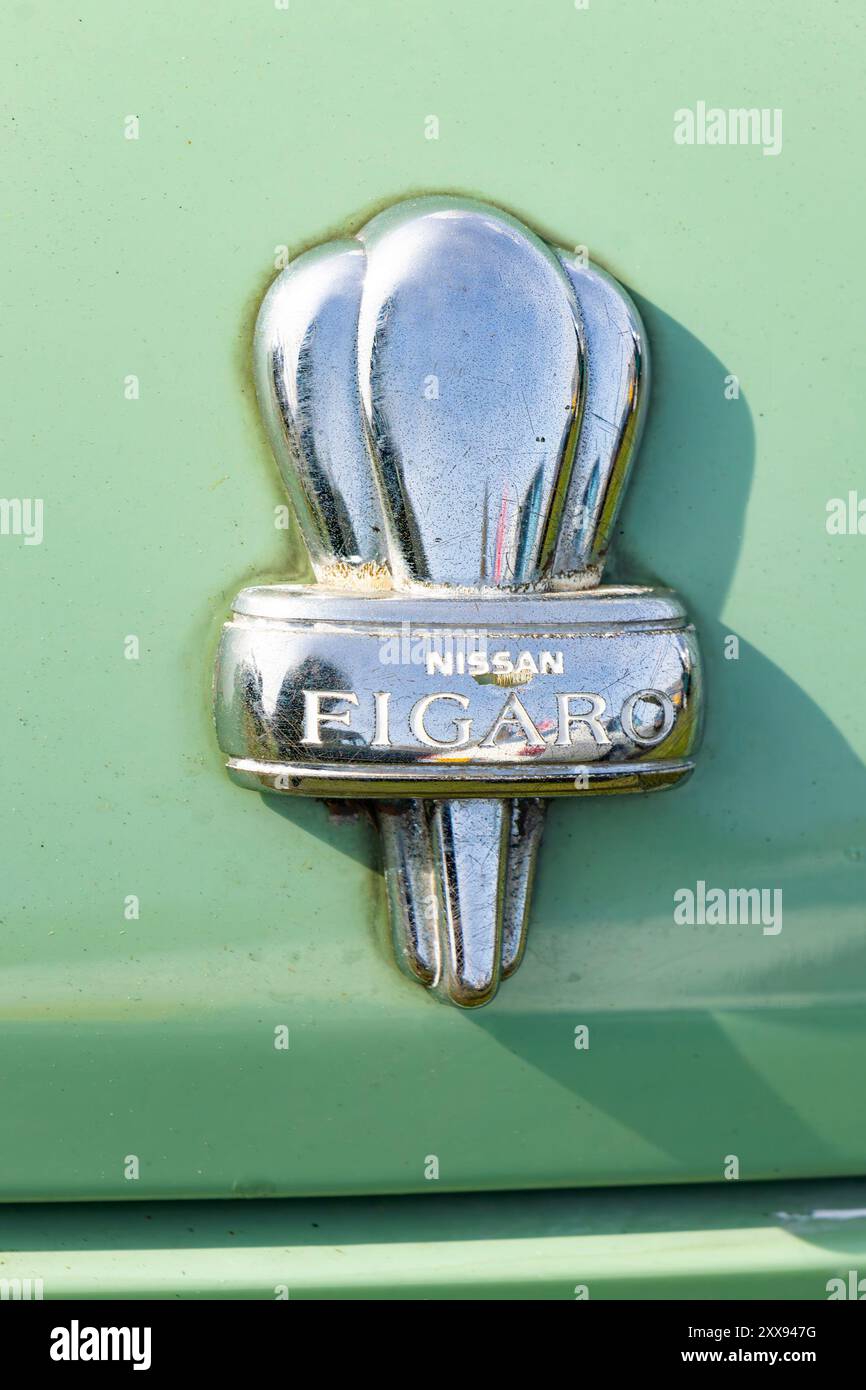 Primo piano di un emblema Nissan Figaro su un'auto vintage verde, che mette in risalto lo stile retrò e i dettagli cromati. Foto Stock