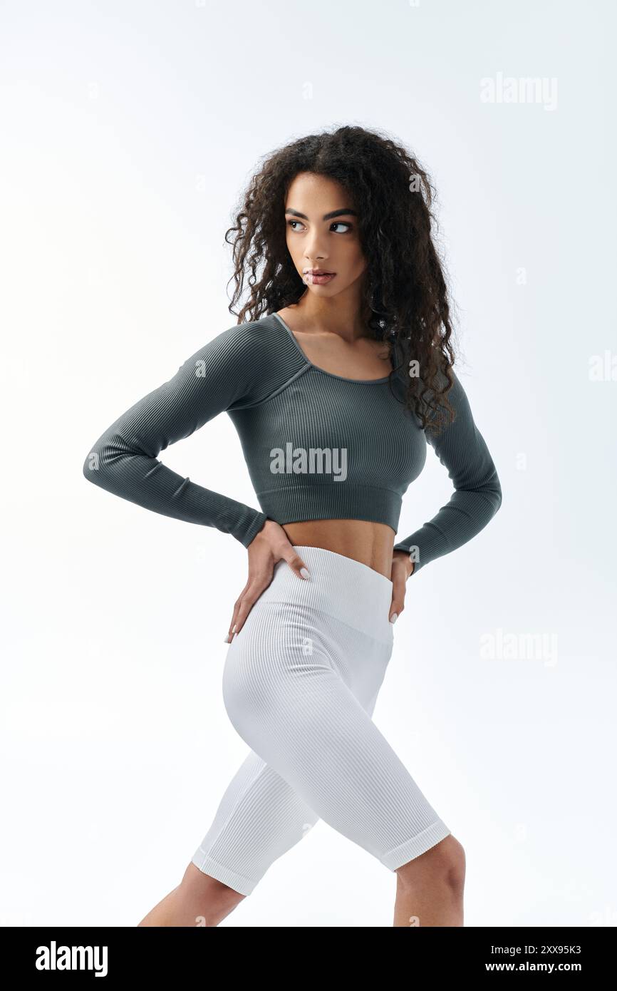 Una giovane e attraente donna afroamericana con pantaloncini bianchi e un top verde si posa in un ambiente da studio. Foto Stock