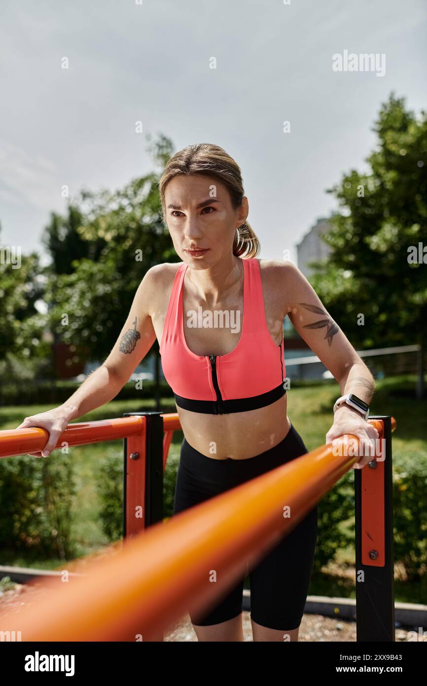 Una giovane donna con la vitiligine, che indossa una cremagliera rosa, lavora su barre parallele in un parco soleggiato. Foto Stock