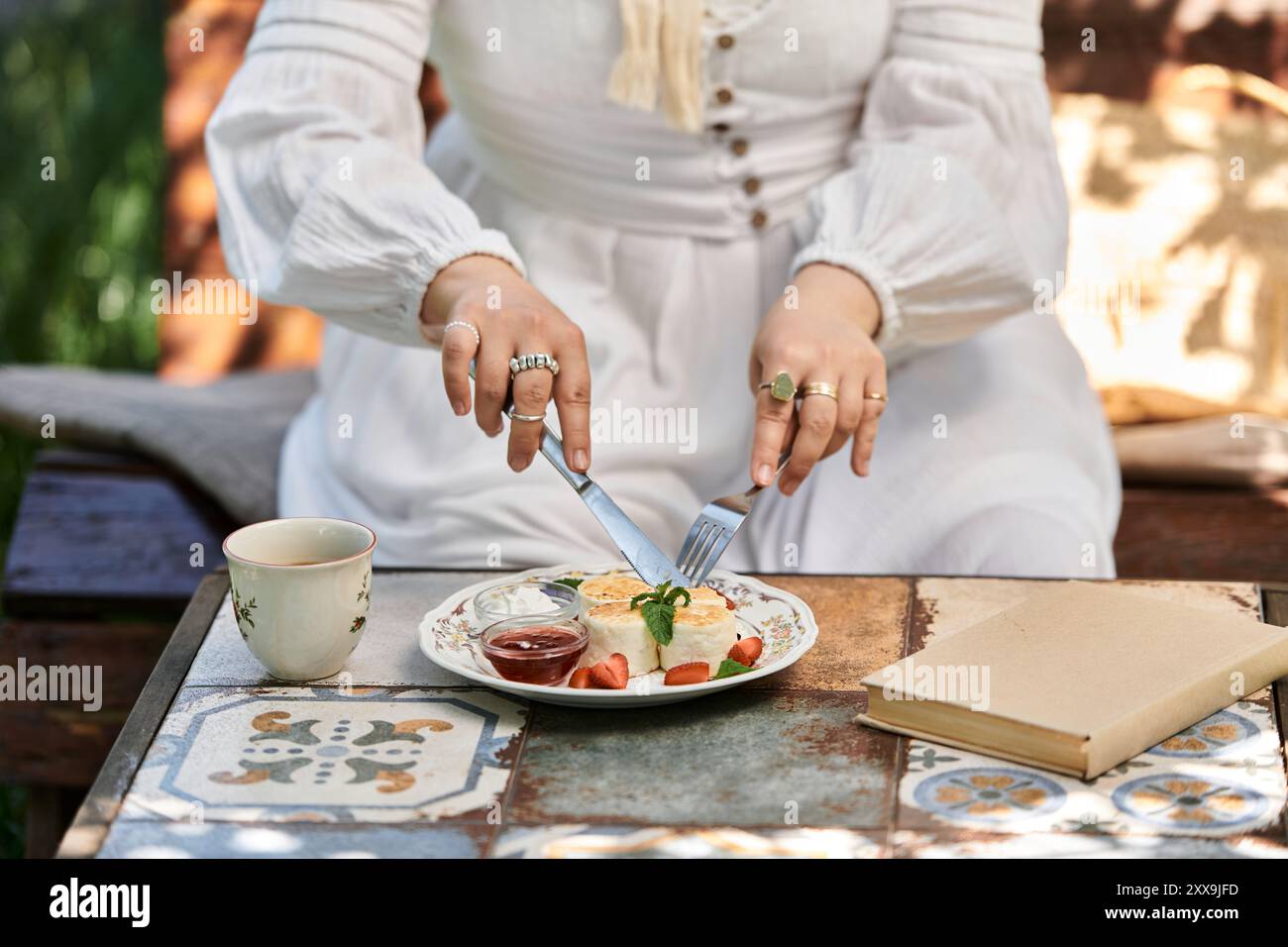 Una giovane donna con un abito bianco gode di un brunch all'aperto in un giardino estivo. Foto Stock