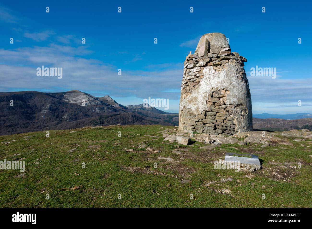 Sulla cima del monte Oketa, antichi simboli di pietra si ergono a sentinella, offrendo vedute panoramiche del lussureggiante paesaggio basco sotto un cielo blu brillante Foto Stock