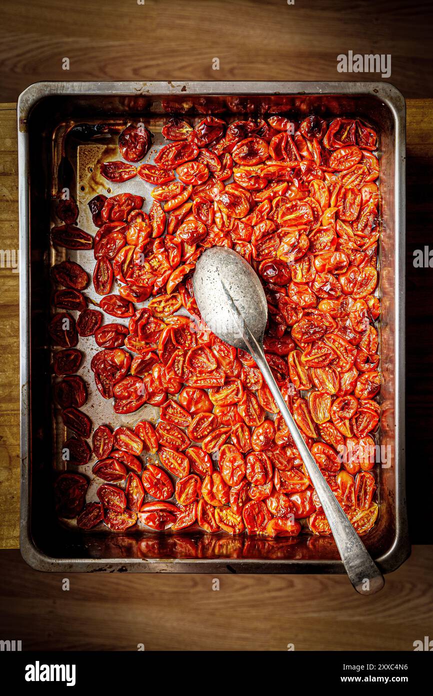 I pomodori ciliegini rossi arrostiti al forno riempiono una teglia da forno in metallo con un cucchiaio d'argento appoggiato sulla parte superiore. Foto Stock