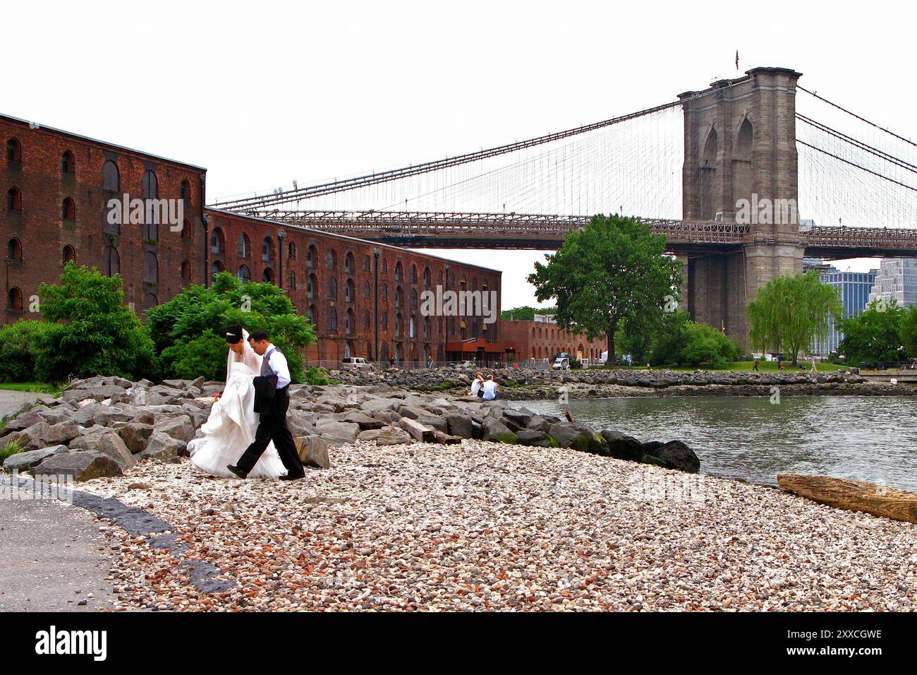 Una coppia di sposi che cammina sulla spiaggia di ciottoli nel Brooklyn Bridge Park nel quartiere DUMBO di Brooklyn Foto Stock