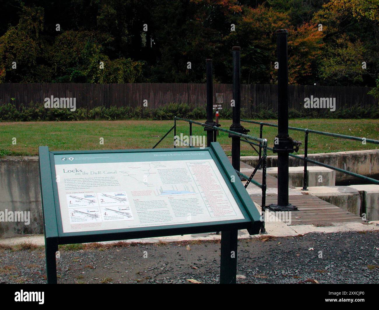 Un prato verde si estende sotto gli alberi ombrosi dietro un segno interpretativo che racconta la storia del Delaware e del Raritan Canal Foto Stock