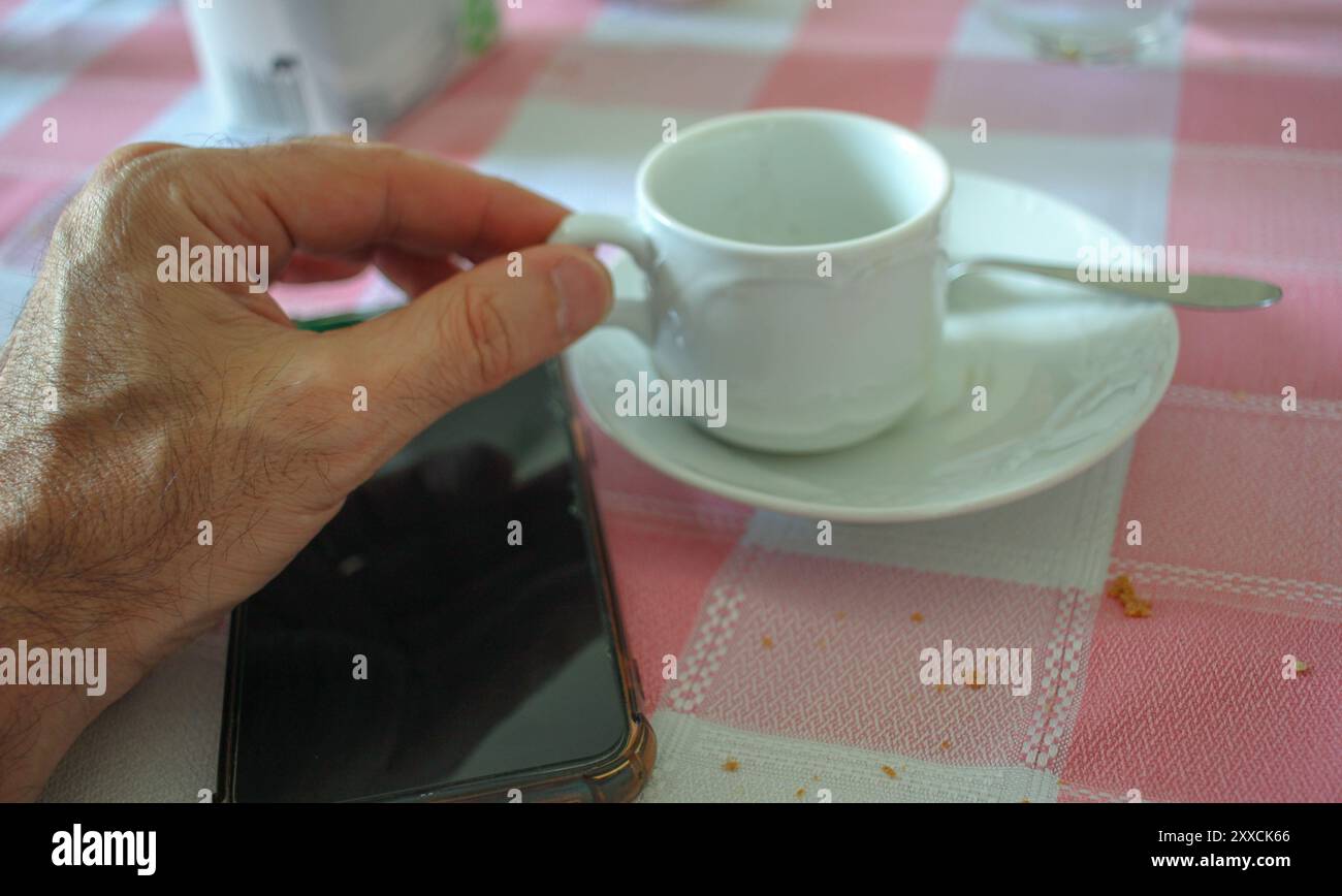 prendere una tazza di caffè a un tavolo con il telefono cellulare a portata di mano per navigare in rete Foto Stock