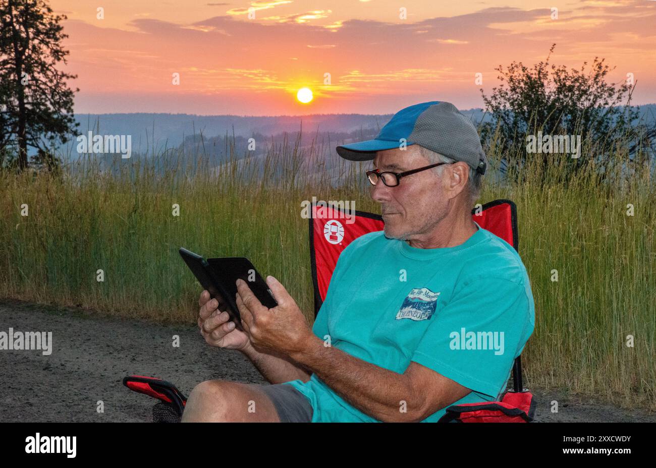 Un maschio adulto si rilassa mentre legge su un libro Kindle a Spring Mountain nella catena montuosa Blue Mountain dell'Oregon centrale. Foto Stock