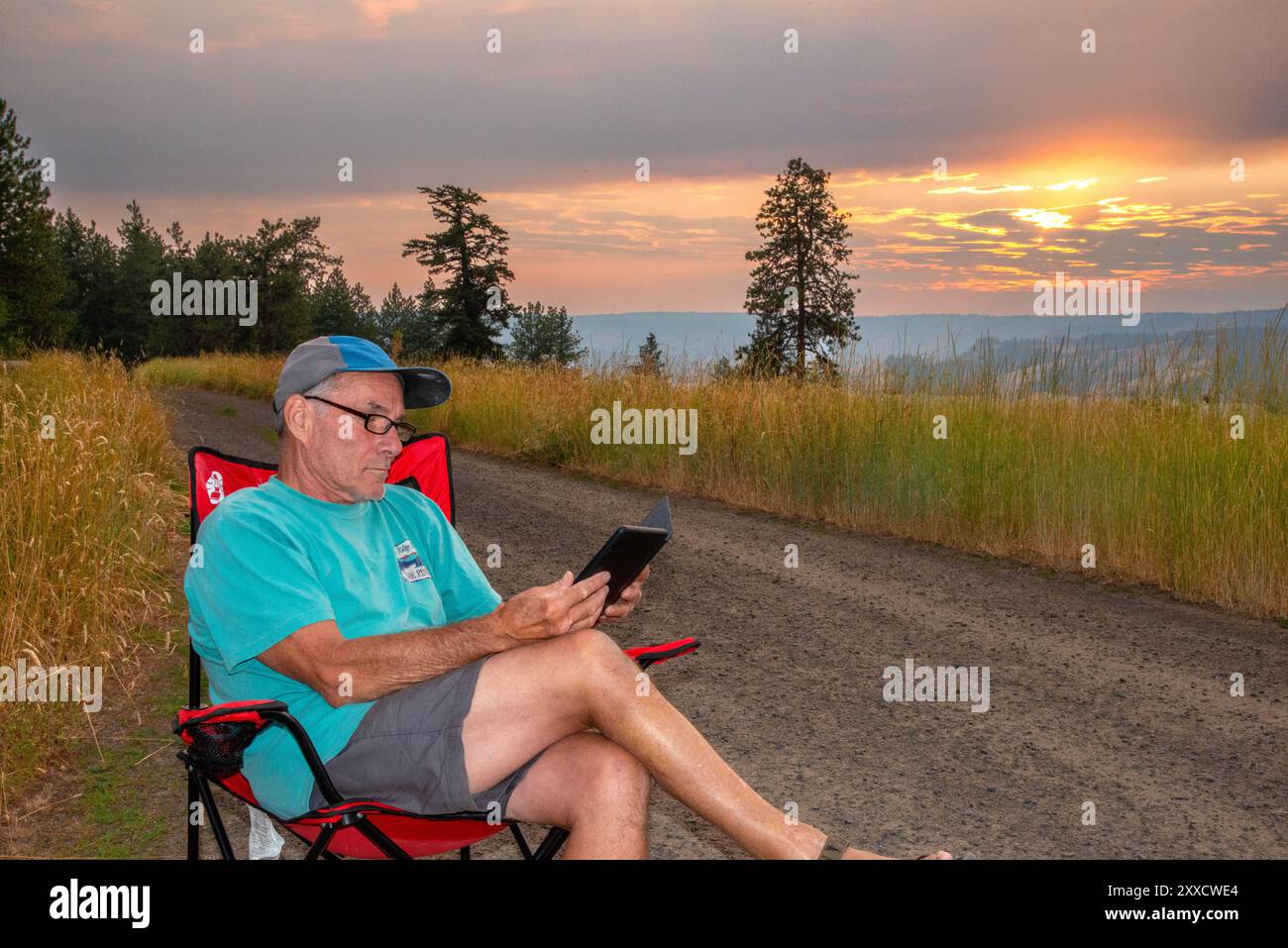Un maschio adulto si rilassa mentre legge su un libro Kindle a Spring Mountain nella catena montuosa Blue Mountain dell'Oregon centrale. Foto Stock
