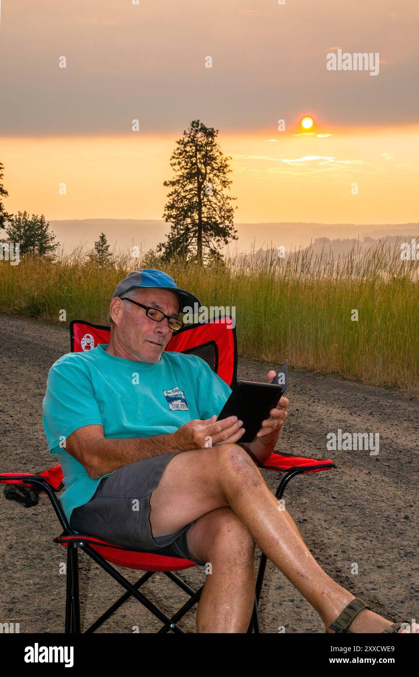Un maschio adulto si rilassa mentre legge su un libro Kindle a Spring Mountain nella catena montuosa Blue Mountain dell'Oregon centrale. Foto Stock